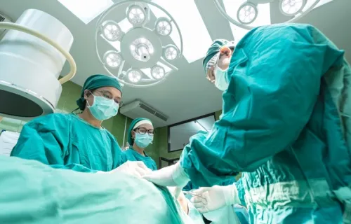 Bild från golvperspektivet i en operationssal där ett antal läkare och sjukskötare i gröna operationskläder och skydd utför en operation