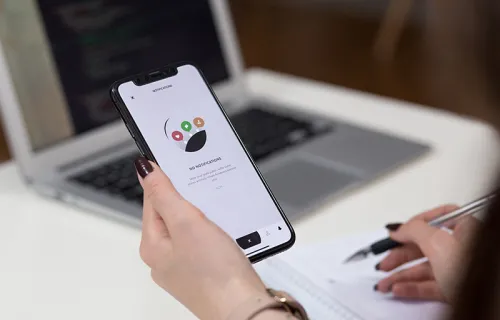 Person håller i en mobiltelefon med ena handen och gör noteringar på ett papper med andra