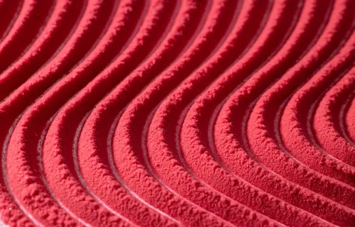 Close-up of a textured red surface featuring a repeating pattern of curved, wave-like ridges.