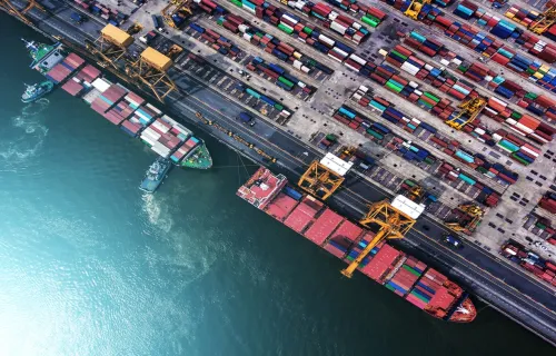 Draufsicht auf einen Hafen mit Frachtschiff und gestapelten Containern, Logistik und globaler…