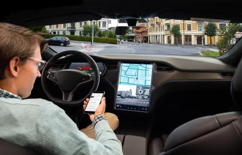 A man in driver seat of a car looking at a smartphone and car GPS