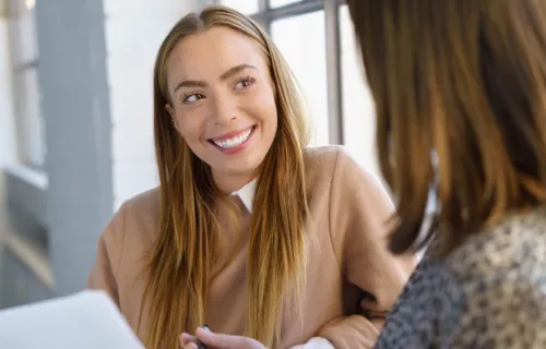 Två kvinnor på kontoret som samtalar. Ena kvinnan håller i ett papper och en penna. 