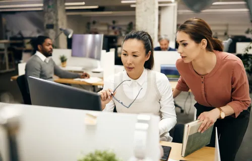 Two businesswomen working collaboratively on a desktop in an office