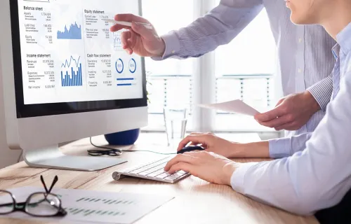 Two colleagues analyzing financial reports on a monitor