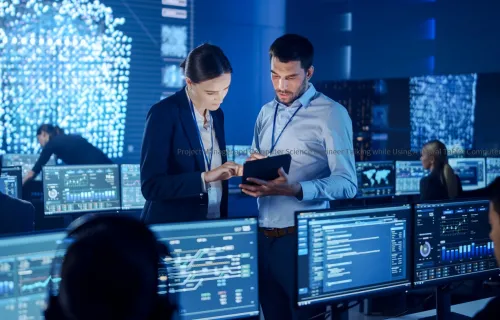 Two cybersecurity professionals discussion information on a tablet in a control room