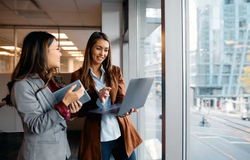 Deux femmes sourient et travaillent devant un ordinateur portable