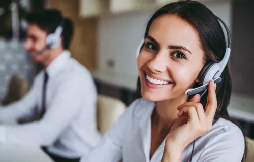 Two people with headsets work in a call centre one smiles at the camera