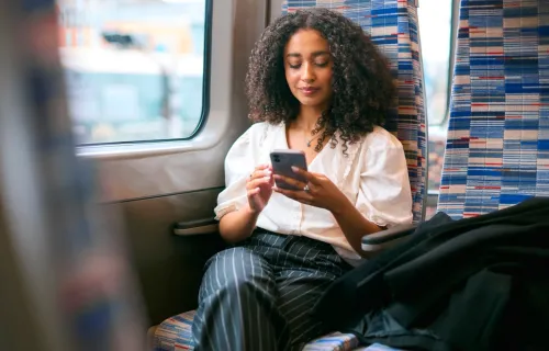 A woman sitting in a patterned train seat by the window using her smartphone
