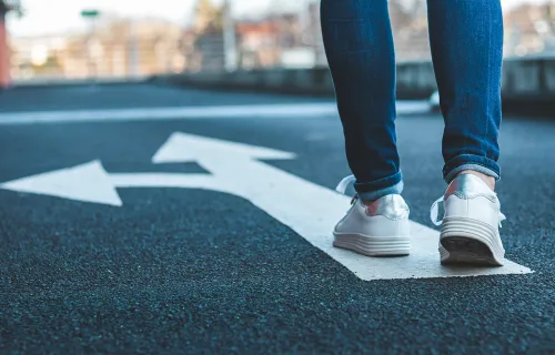 Eine Person geht auf einer Straße an einer markierten Abzweigung entlang, passend zum Thema…