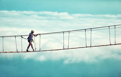 Eine Person geht über eine Hängebrücke über den Wolken