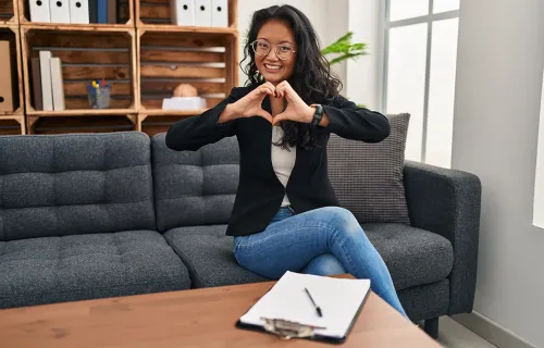 Woman sat on sofa making heart symbol with her hands