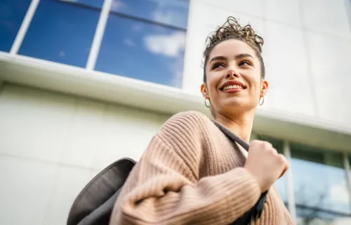 Kuvituskuva: opiskelija hymyilee yliopistorakennuksen edessä.