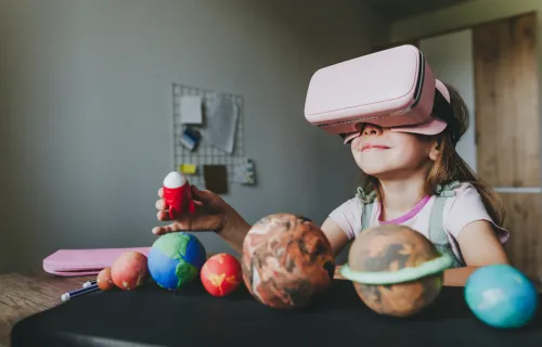 Young girl surrounded by models of planets uses VR headset
