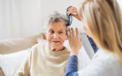 A health visitor combing hair of senior woman at home