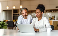 a man and a woman working on their computer in the kitchen