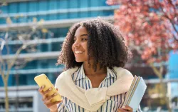 Personne tenant un téléphone portable debout devant un bâtiment et des arbres