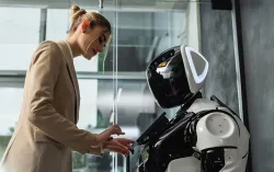 Une femme en blazer interagit avec un robot humanoïde dans un bureau.
