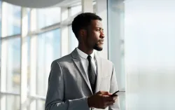 Consultant stood looking out of a window with a mobile device
