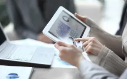 Close up of two people holding a digital tablet looking at a report with several graphs