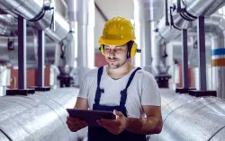 Male worker wearing hardhat looking at a tablet in manufacturing plant