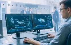 Male data scientist looking at two computer screens car factory