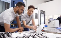 female and male coworkers in a factory lab looking at a laptop