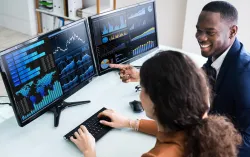 two consultants looksing at data together on two monitors