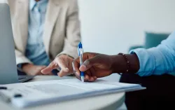 consultant taking notes on paper beside a laptop