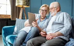 elderly couple sat on sofa looking at tablet device together