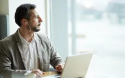 Man sat at laptop with headphones on looking out window