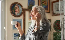 Smiling woman standing and talking on phone while holding cup