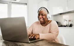 woman sitting in kitchen using laptop wearing white headphones