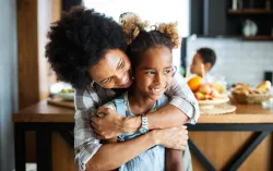 young girl and parent or guardian embracing in kitchen