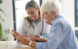 Doctor showing elderly patient how to use NHS booking system on tablet device