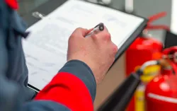 Personne avec presse-papiers debout devant deux extincteurs
