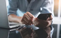Personne devant un ordinateur regardant un téléphone portable.