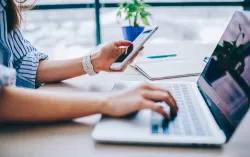 Espace de travail numérique avec un ordinateur portable, un téléphone et un carnet sur le bureau.