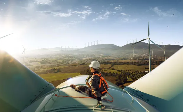 engineer sitting on top of a wind turbine looking at a sunset landscape