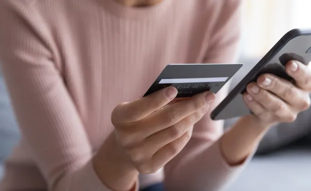 Person holder bankkort og mobiltelefon for digital betaling.