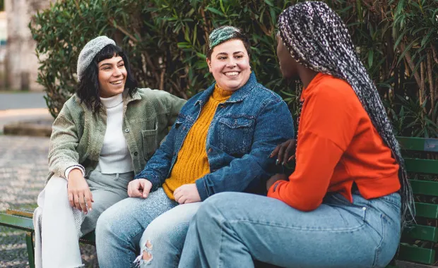 three people talking outside and laughing on a bench
