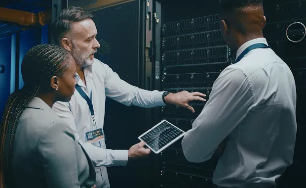 Three cybersecurity professionals using a tablet in a server room