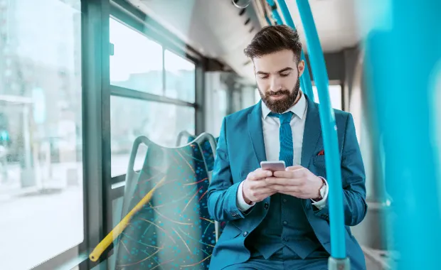 Kuvituskuvassa mies istuu bussissa mobiililaitetta selaten