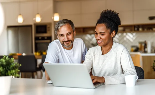 a man and woman in their kitchen looking at a computer