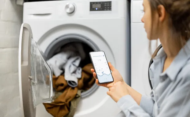Woman looking at her phone sat next to an open washing machine