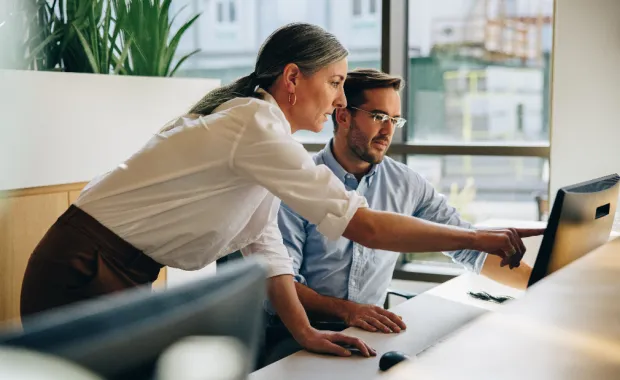 Deux professionnels collaborent devant un ordinateur dans un environnement de bureau.
