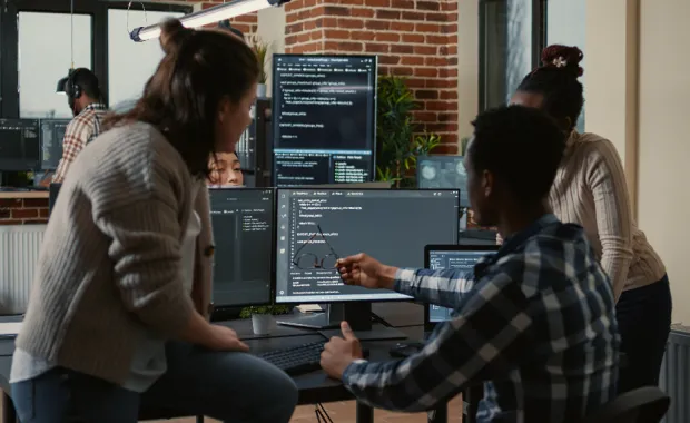developers gathered round a desktop with code on the monitor