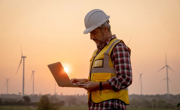 A man wearing a high-visibility jacket and a hard hat using a laptop