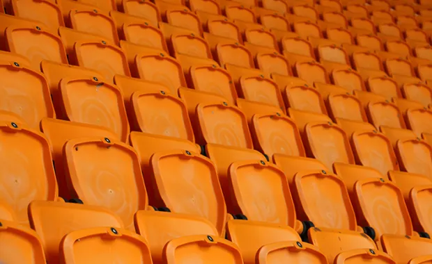 Rows of vacant orange fold down seats at a sports stadium