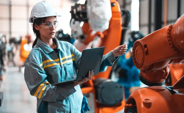 Technicienne équipée d’un casque de sécurité utilisant une tablette à proximité d’un bras robotisé dans un environnement industriel
