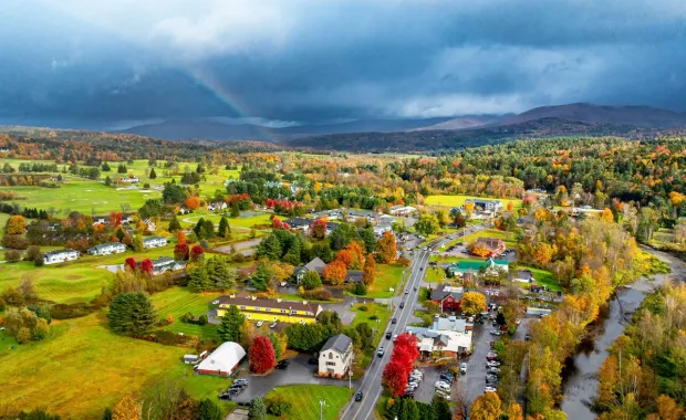 Aerial view of a rural town with autumn foliage and storm clouds over mountains